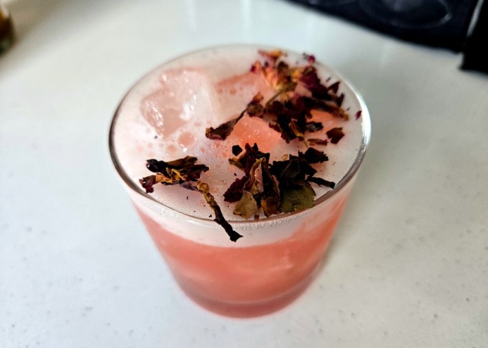 A pink drink garnished in dried hibiscus flower, with foam and ice on top.