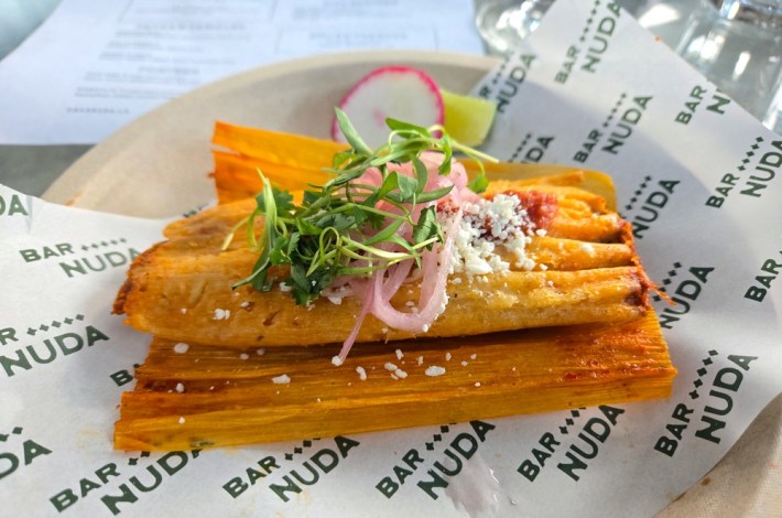 A Cotija-and-cilantro-topped tamal on a paper that says Bar Nuda many times
