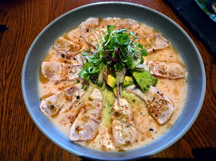 A dish of sashimi-style yellowtail crudo in a pale yellow sauce.