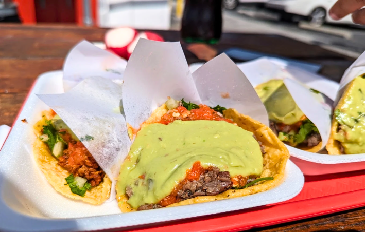 Tacos estilo Tijuana topped with guacamole and a spicy red salsa.
