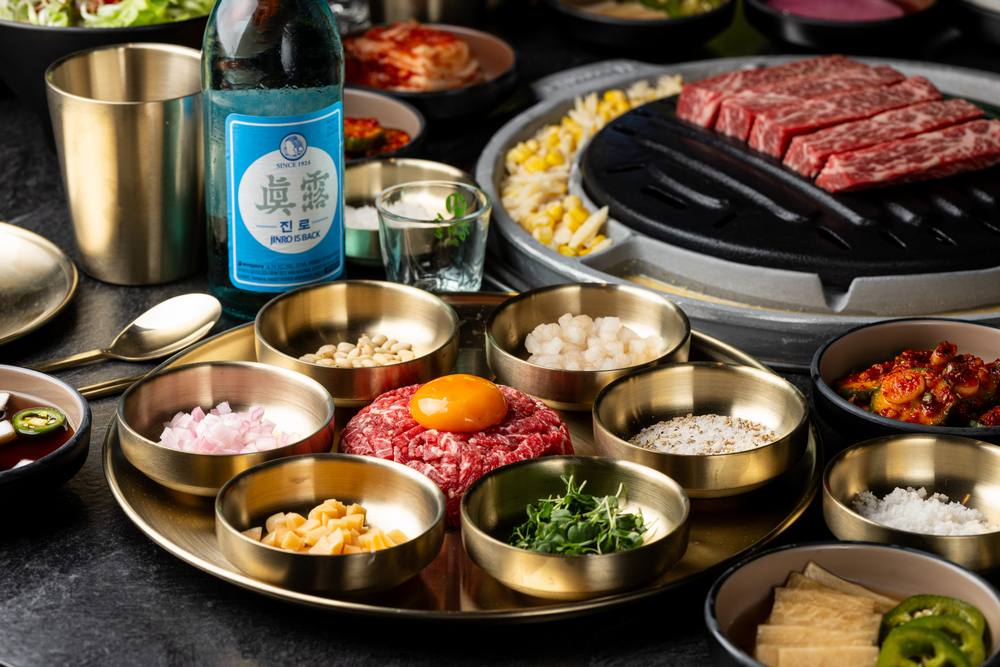 Baekjeong's beef tartare with boneless short rib behind it on the grill and a bottle of soju beside it.