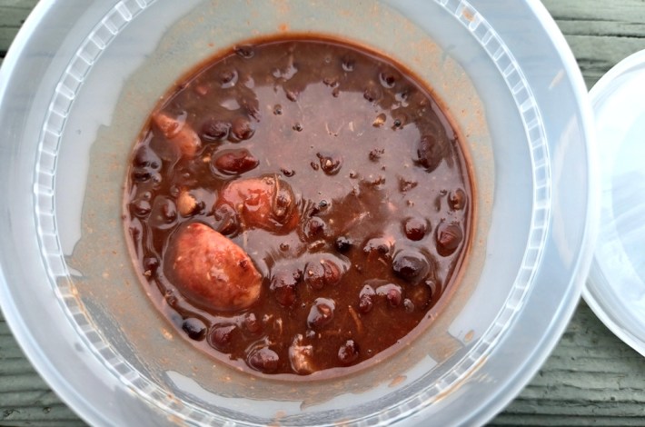 A plastic container containing the Brazilian staple feijoada, with sausage visible at the top.