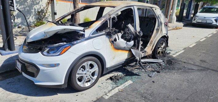 A burned out BlueLA car parked at a station. The interior of the car is almost completely destroyed.
