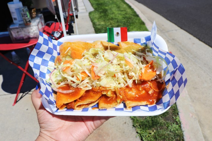 An order of tacos de canasta topped with a mix of shredded lettuce, purple onion and pickled carrots. And dressed with both green and red salsa.