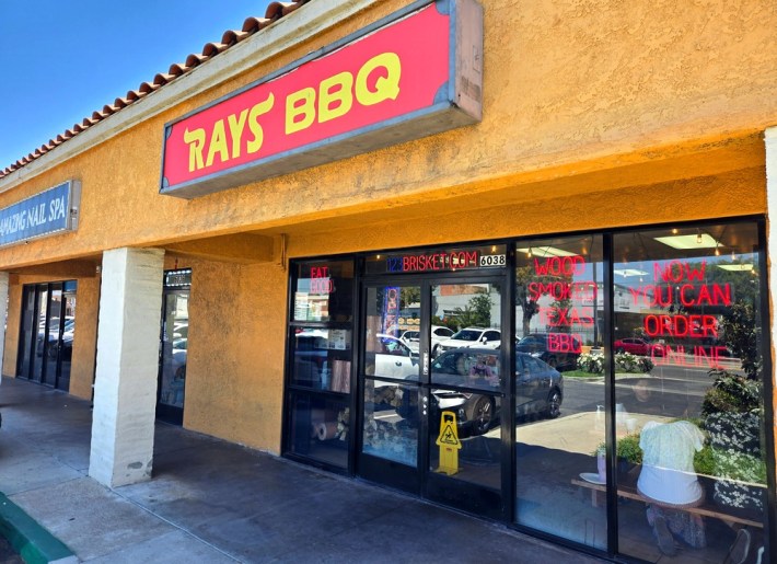 An exterior of Ray's BBQ in Huntington Park, with a red sign and red neon over orange walls.