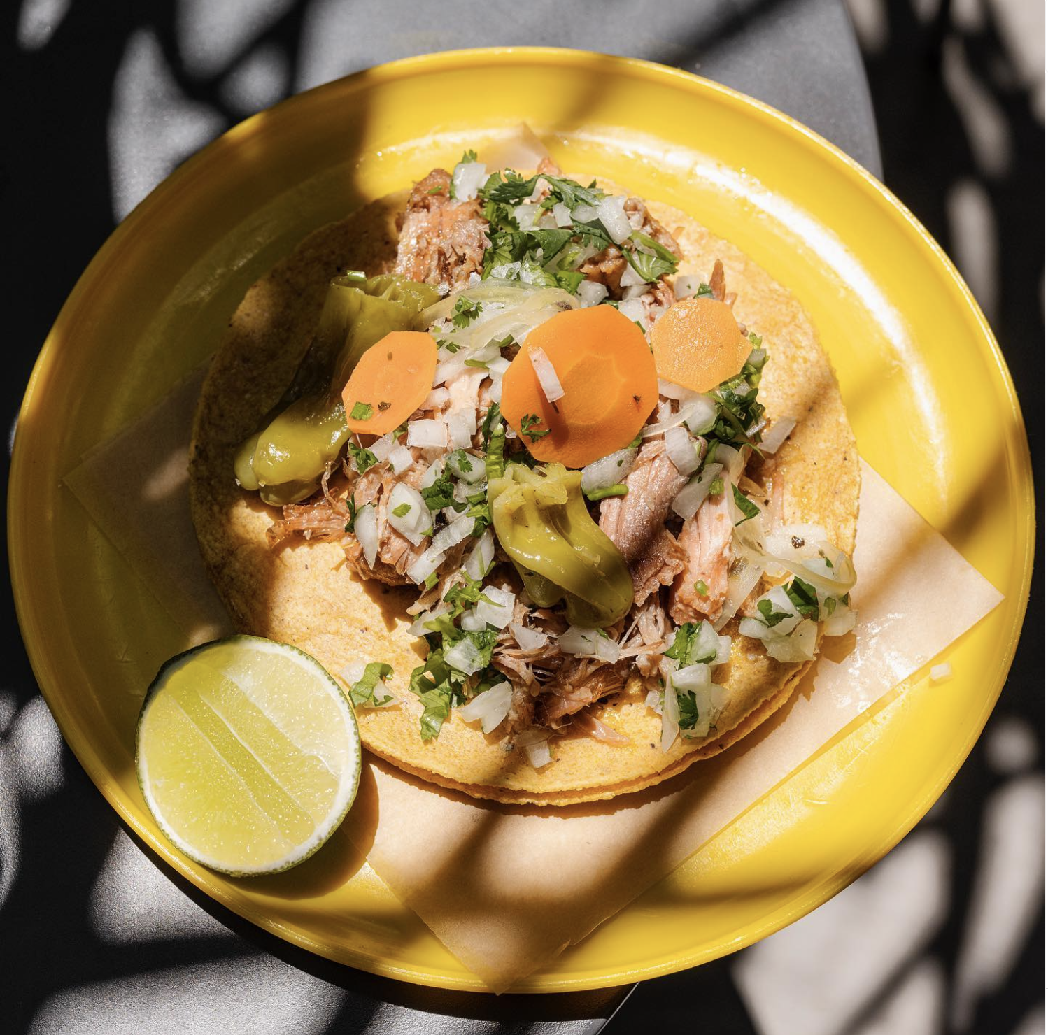 Taco de carnitas on a bright yellow plate.