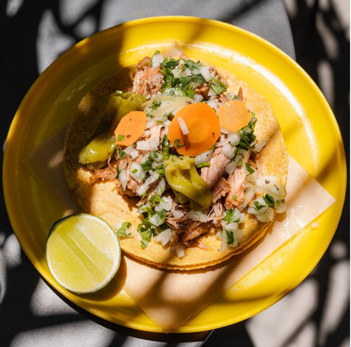 Taco de carnitas on a bright yellow plate.