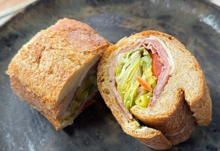 A sandwich cut in half showing lettuce, tomato, ham, pepperochini, and cheese