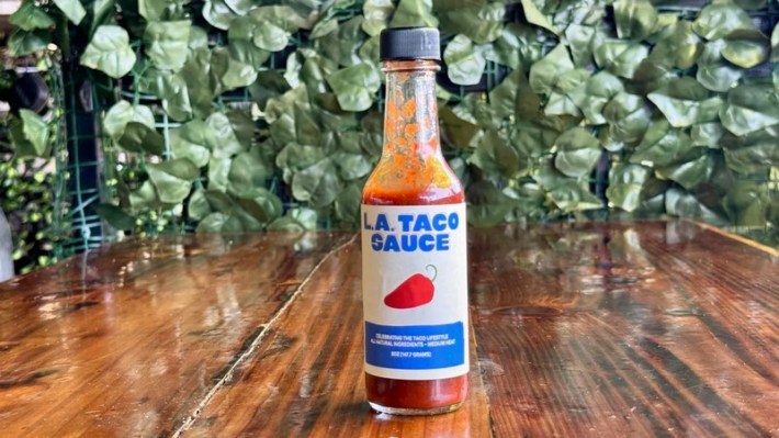 A bottle of red-colored hot sauce with L.A. TACO Sauce on the label and a drawing of a red chile