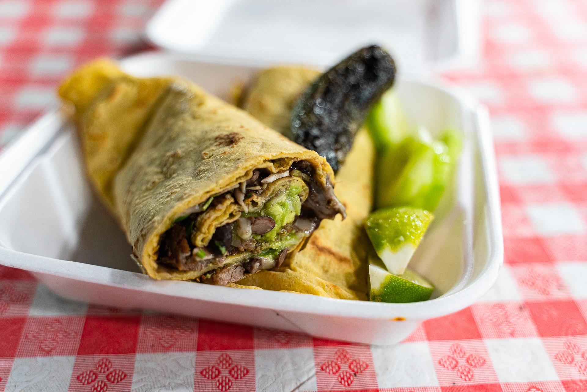 El Taco 5 y 10, large corn tortilla wrap cut in half and filling a styrofoam container with a grilled jalapeño laying on top and lemon wedges on the side.
