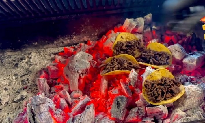 Four tacos sitting directly on the hot coals of a grill