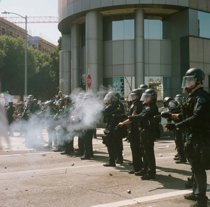 A line of cops shoots tear gas at unseen protestors