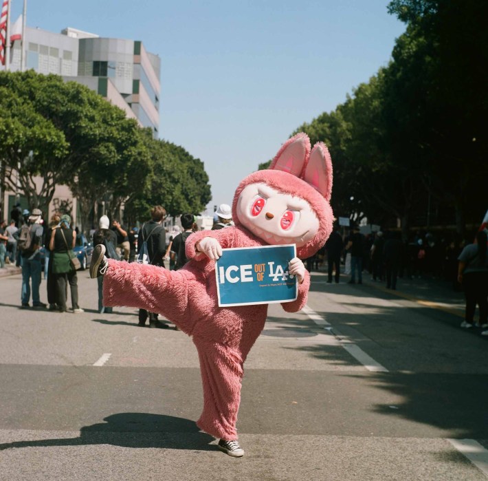 A person in a pink Labubu costume holds a sign that says "ICE out of LA"