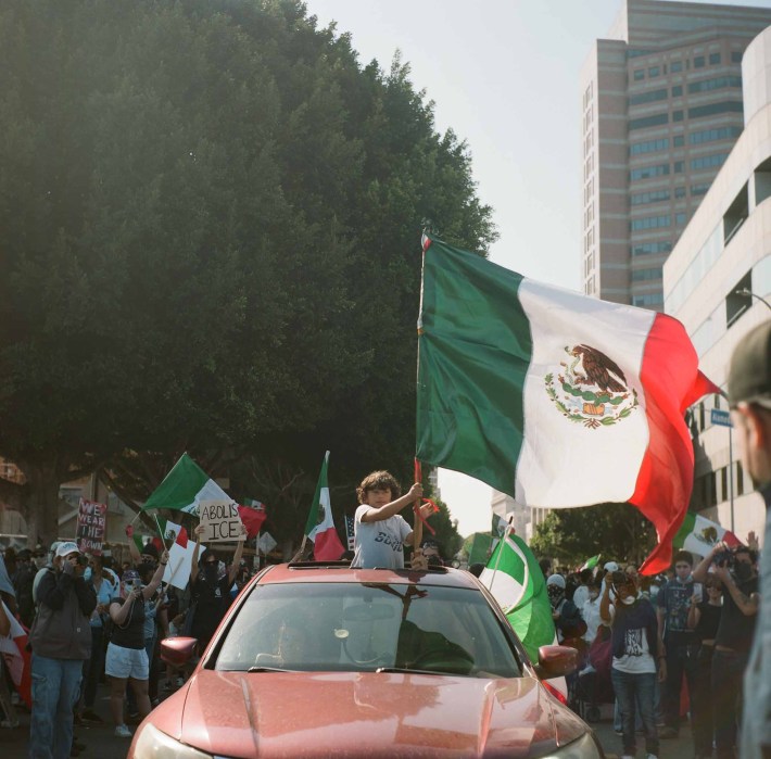 A child waves a Mexican flag from the sunroof of a red car amid a crowd of people