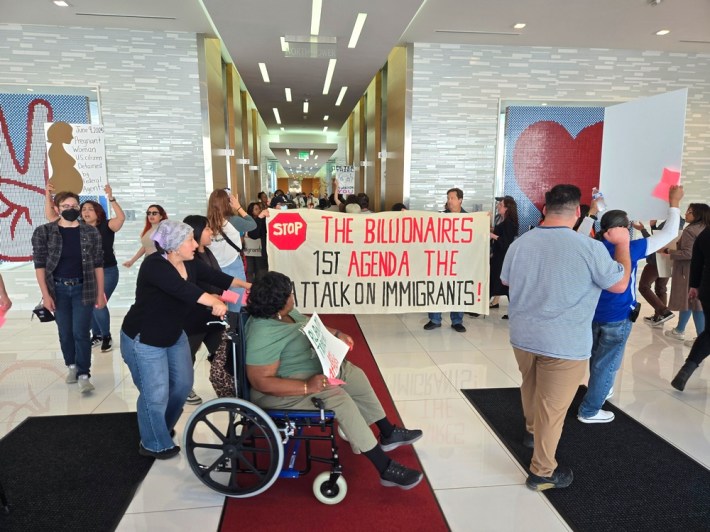 Protestors circling inside a building's lobby building while others hold up a large sign