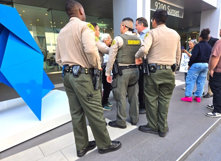 Sheriffs deputies standing in a circle talking to an older woman on the stairs of an office building