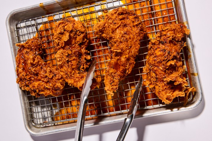 Four crispy chicken tenders with craggy skin over a cooking grate, with pooling orange juices underneath