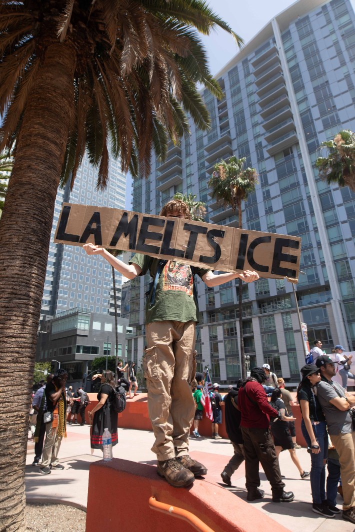 A person holds a cardboard sign that says "LA MELTS ICE"