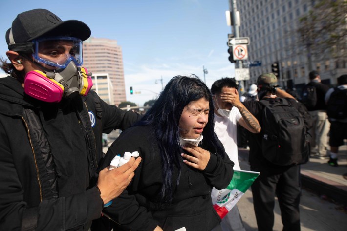 A woman chokes on tear gas as someone holds her, other protestors on her side holding their eyes