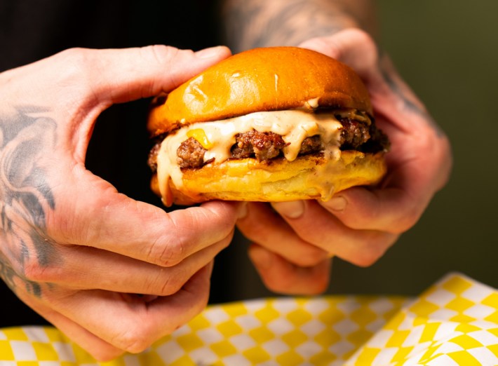 Inked hands hold a cheeseburger at Boho Burgers & Brats.