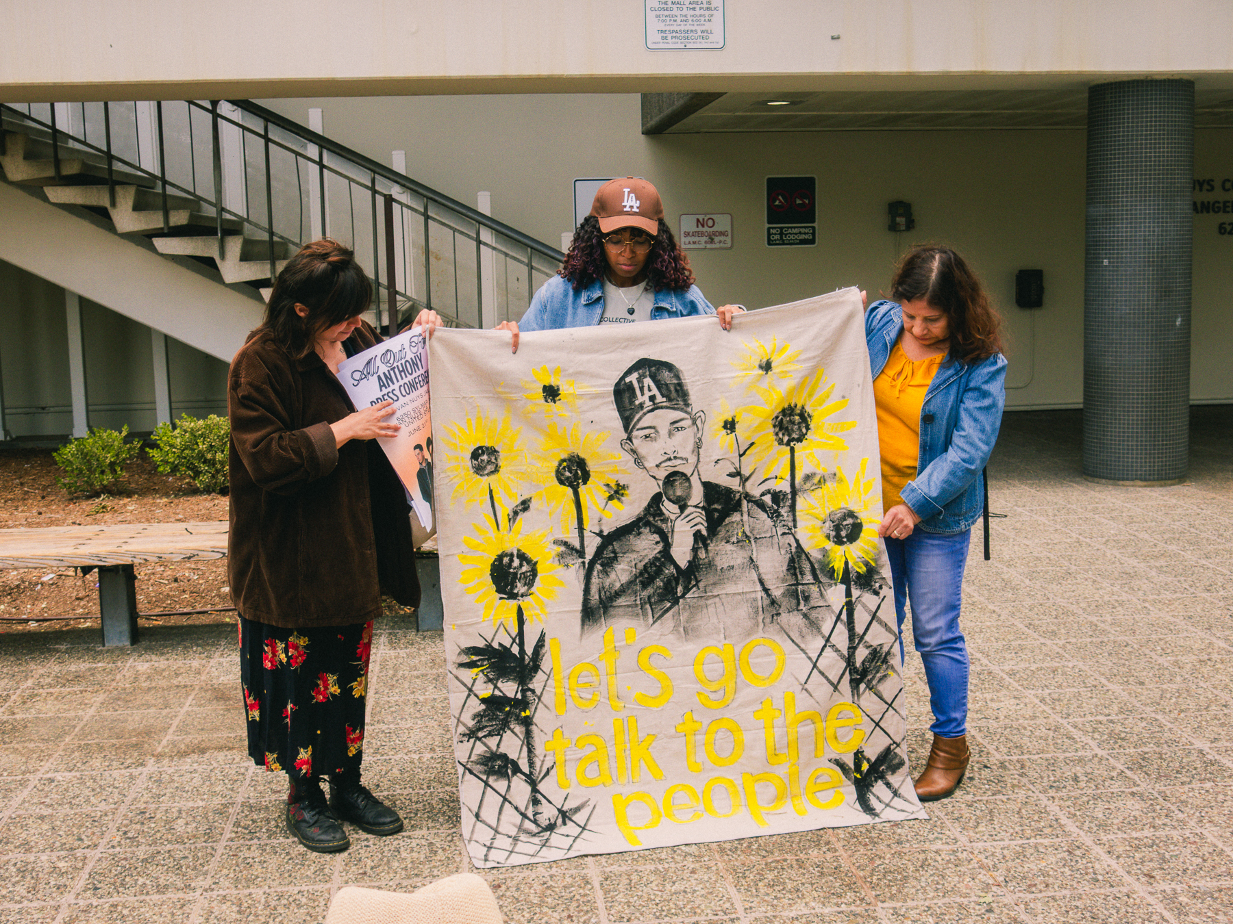3 people hold up a sign with illsurated sunflowers and the face of jailed journalist Anthony Ordenoff
