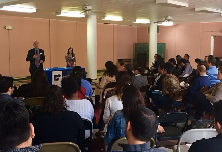 A room full of people watch as two speakers present an educational seminar
