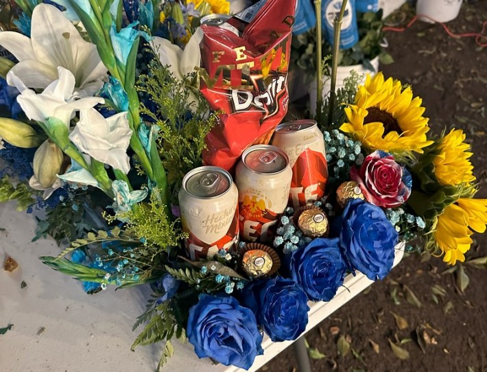 A white plastic table set with snflowers, blue flowers, beer cans, and a bag of Doritos