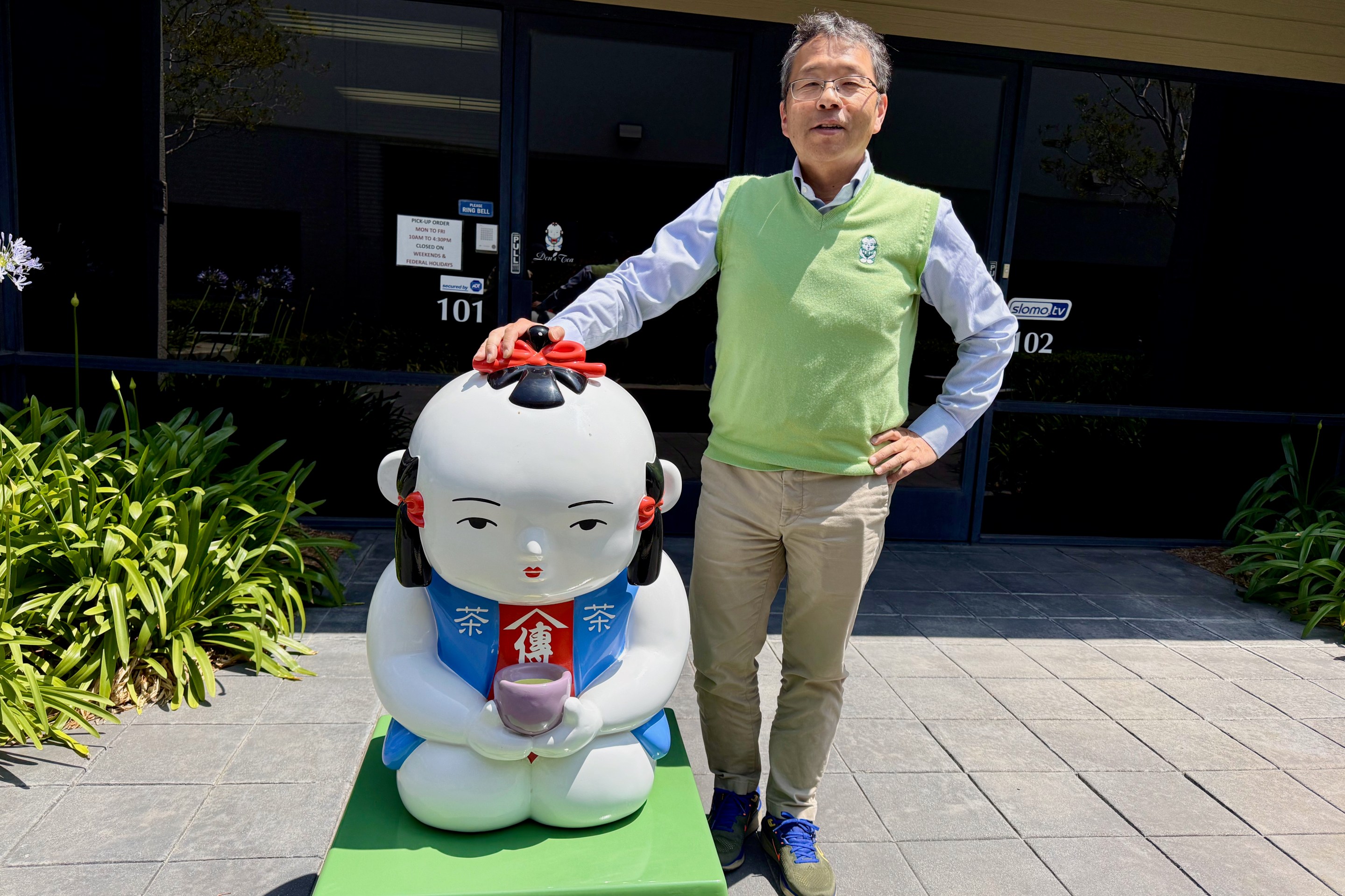 Den of Den's Tea posing next to their mascot.