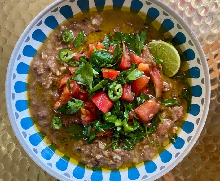 A blue paper bowl with lentil stew topped with jalapeno, tomato, and cilantro.