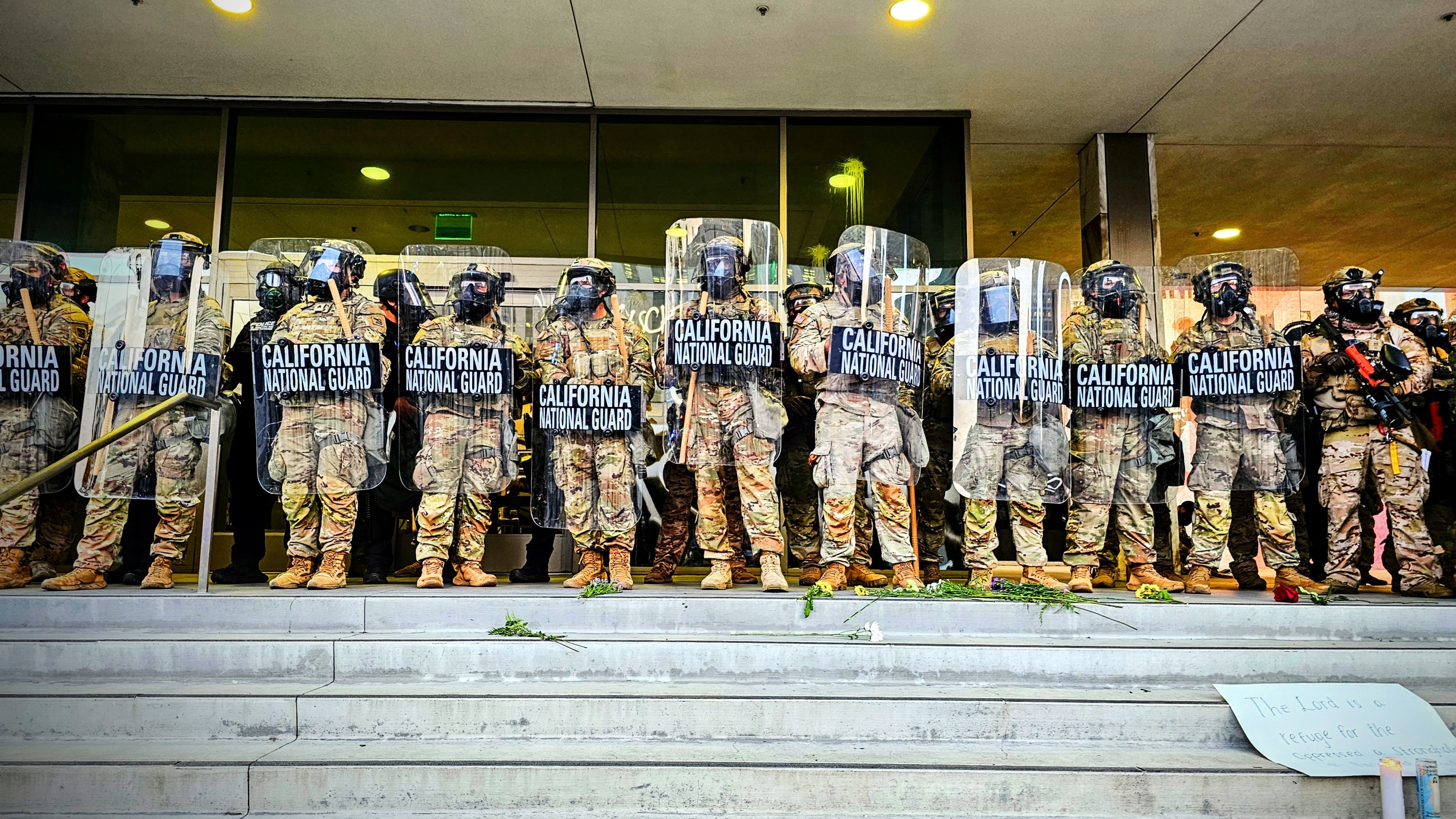 A line of Nationa Guardsmen stand in at the top of a short staircase holding riot shields.