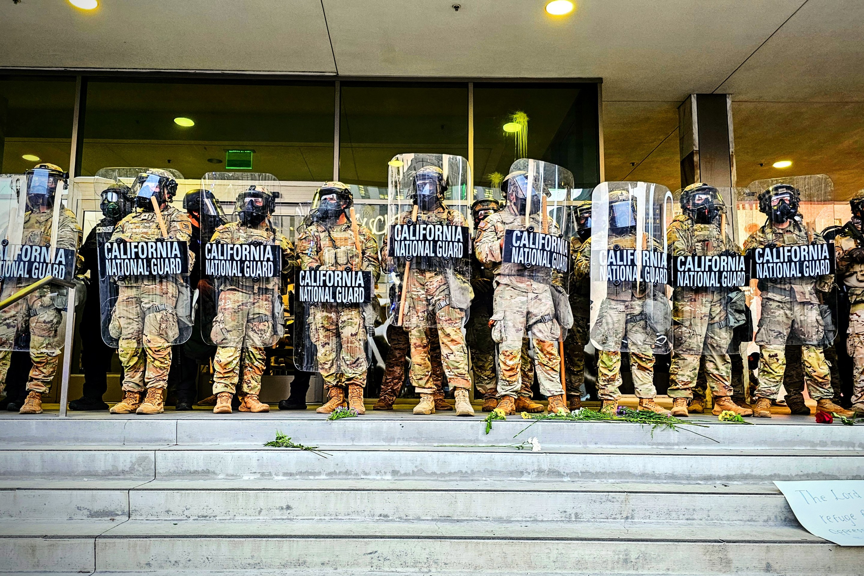 A line of Nationa Guardsmen stand in at the top of a short staircase holding riot shields.