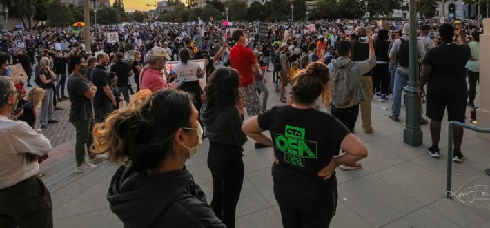 A large crowd of people gathered at a demonstration, their backs towards the camera