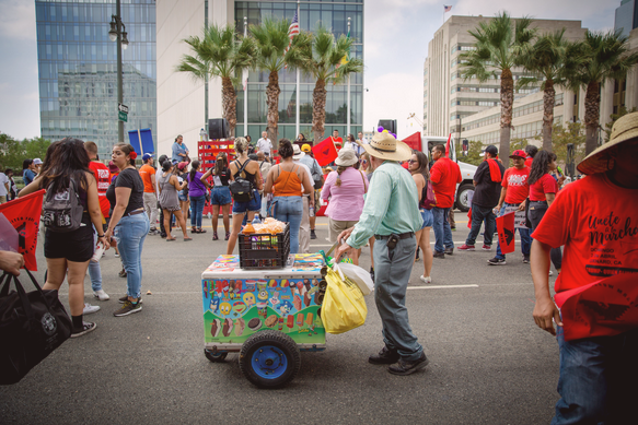 An ice cream vendor and his cart moving through a crowd of demonstrators, many of whom wear red shirts