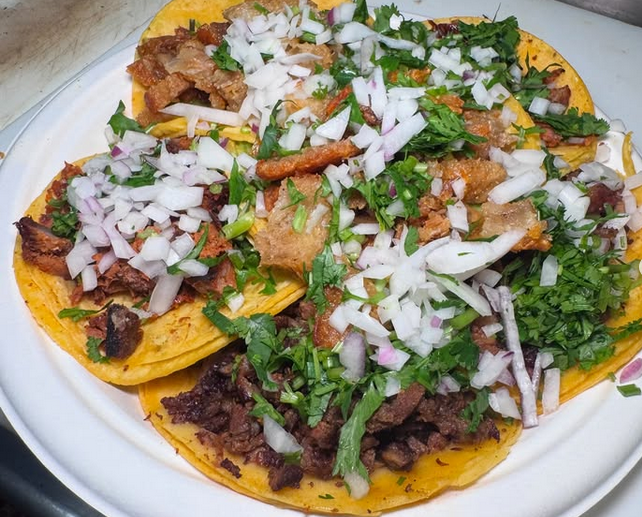Asada and chicken tacos from El Fogon, covered in onions and cilantro on corn tortillas.