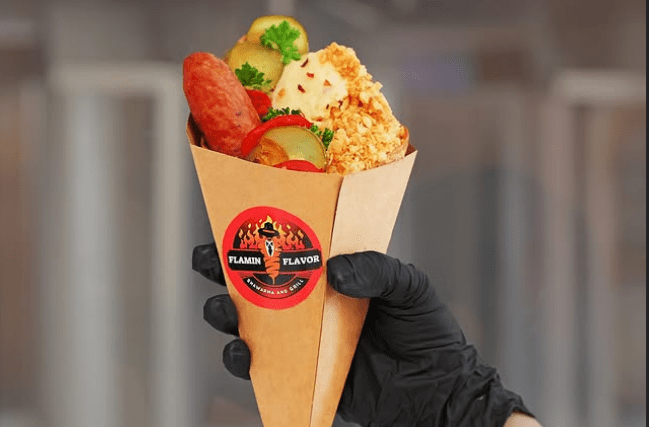 A cone with sausage, tortilla, crispy potatoes and other vegetables being held by a black gloved hand