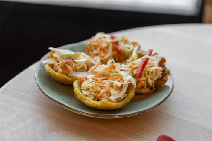 Four Haitian plantain cups with pickled root vegetables, on a plate.