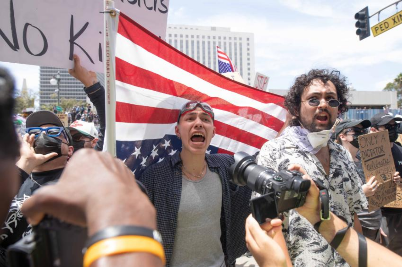 A protestor shouts holding an upside down U.S. flag behind him