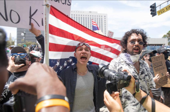 A protestor shouts while holding an upside down U.S. flag behind him