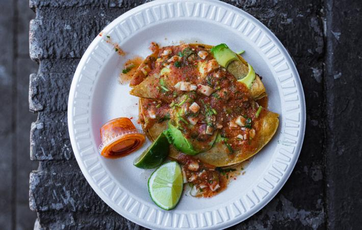 a plastic plate with a taco dorado smothered in salsa and avocado with lime and a cup of red salsa
