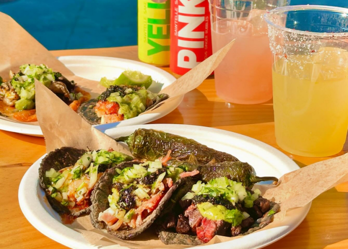 Two plates of tacos in front of poured drinks next to their cans