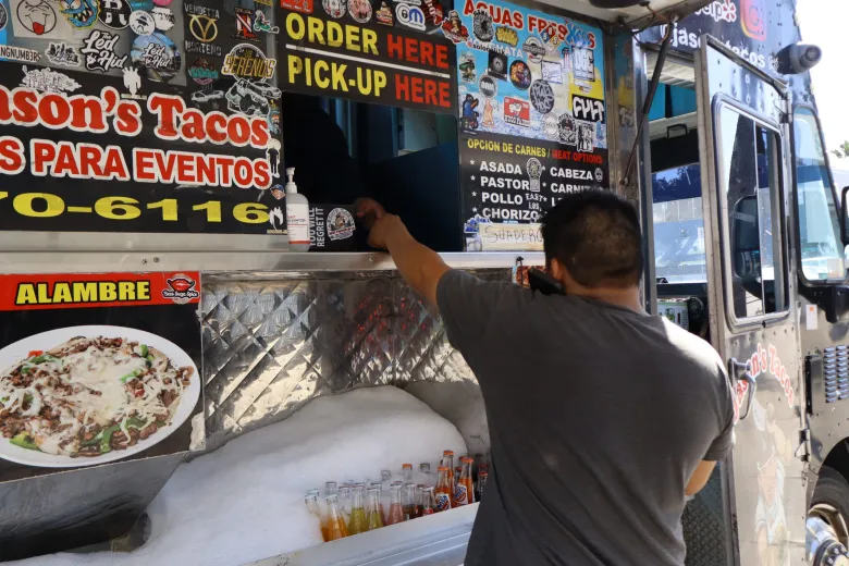 A customer picks up an order from the heavily stickered window at Jason’s Tacos in East L.A.