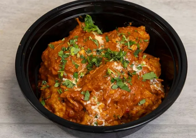A bowl of orange butter masala momo dumplings topped with herbs