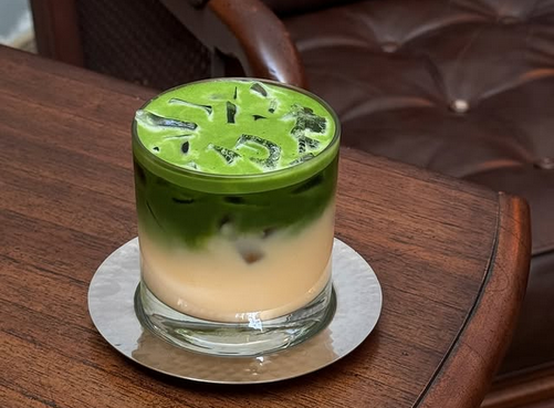 A cantaloupe milk matcha in a glass, its top a bright green, its bottom half a milky tan color