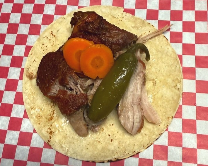 A taco de carnitas with a pickled jalapeno pepper and carrots on a corn tortilla