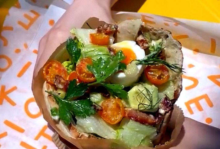 A pita sandwich showing parsley, egg, cherry tomatoes, dill, and avocado.
