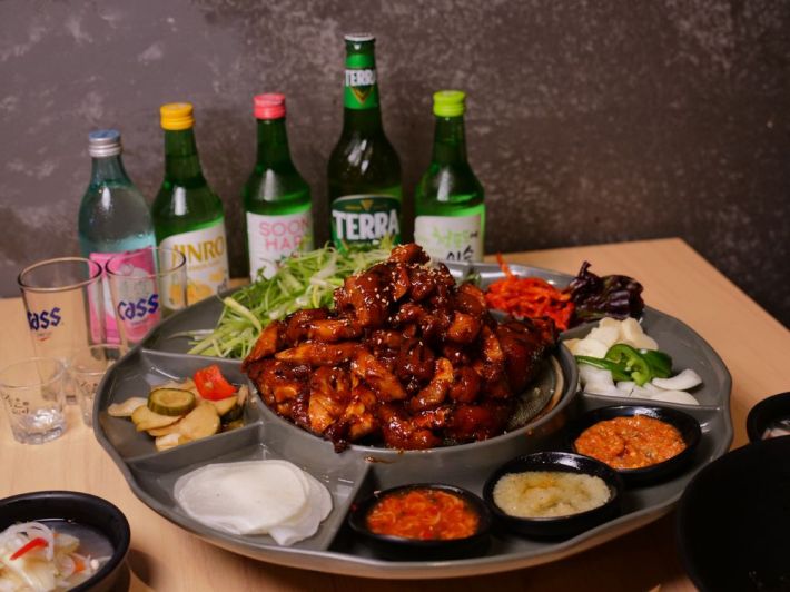 A platter of jokbal surrounded by Korean banchan and sauces, with five bottles of sochu behind it