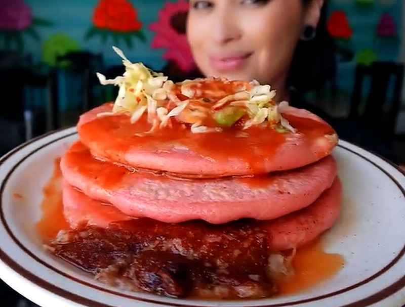 A stack of 3 pink pupusas topped with cabbage and with cheese coming out