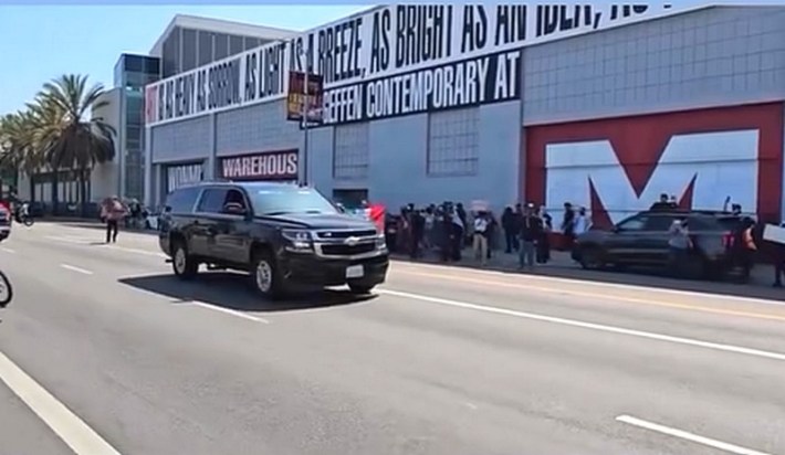 A black SUV drives with protestors on its right, next to L.A.'s MOCA building