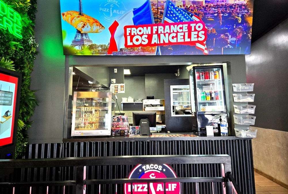 A counter with a televised sign above it that shows the Eiffel Tower next to an overview of Los Angeles, and says "From France to Los Angeles"