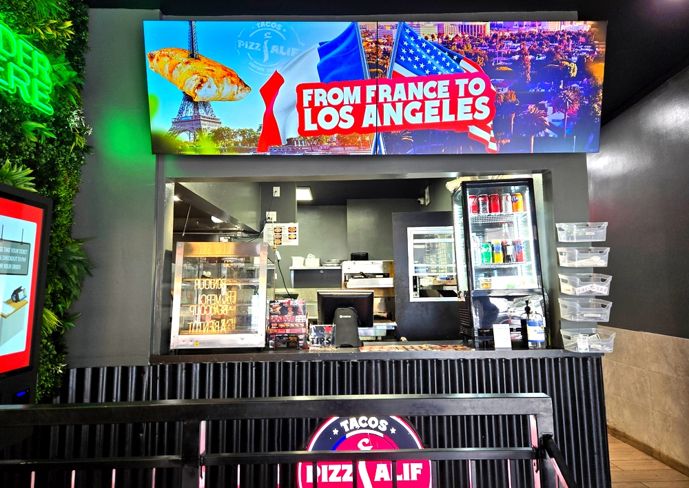 A counter with a televised sign above it that shows the Eiffel Tower next to an overview of Los Angeles, and says "From France to Los Angeles"